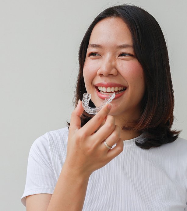 Smiling patient holding clear aligner